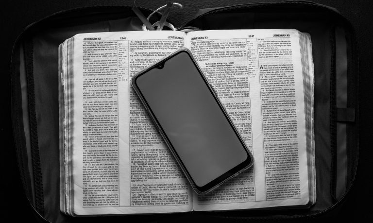 An open Bible next to a phone on a kitchen table — is AI the devi