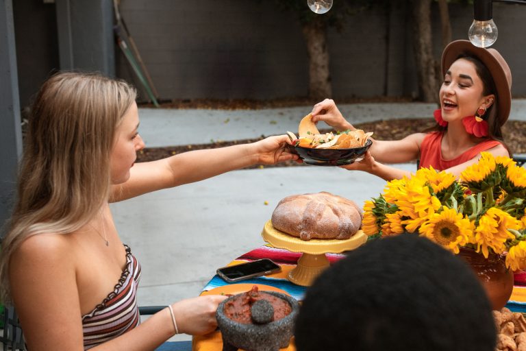 Friends passing food across a table set with sunflowers and pan dulce — a prayer for Hispanic Heritage Month